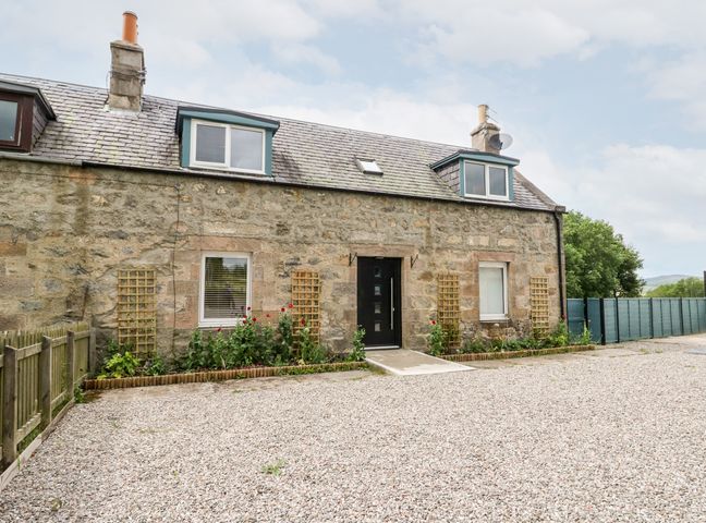 A stone house with two dormer windows a black door flower beds and gravel driveway at Ulla Dhu in Nethy Bridge