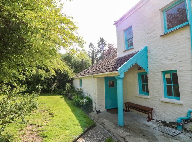 A white cottage with turquoise window frames and door next to a grassy garden with bushes at Parke Cottage in Henllan Amgoed near Whitland
