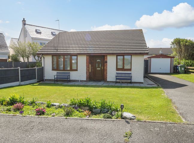 A single story house with two benches outside and a driveway leading to a garage at Aurora in Trearddur Bay
