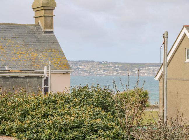 A view of rooftops bushes and a sea with a town in the background at Driftwood in Marazion