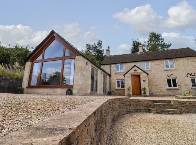 A stone house with a large window extension and a gravel driveway at The Nook in Jack's Green near Painswick