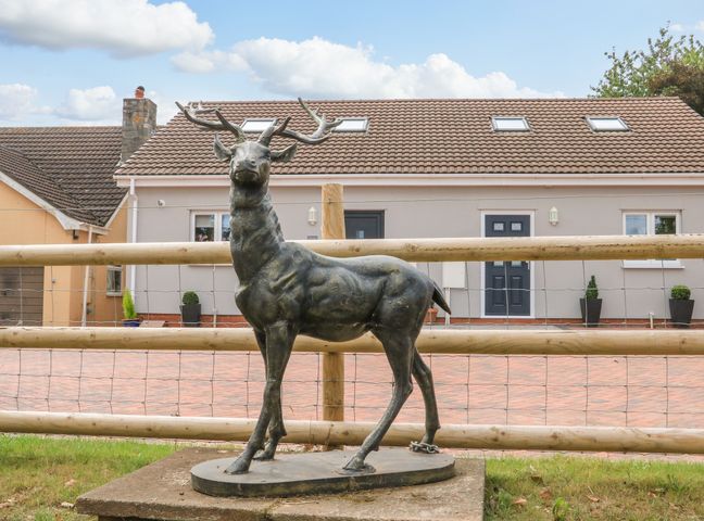 A metal stag statue on a stone base in front of a fenced yard with a house in the background at Sawtons Cottage 1 in Dawlish