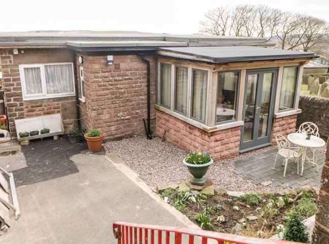 A small garden area with a stone patio table and chairs outside a stone building with large windows at The Netty in Quarnford near Buxton