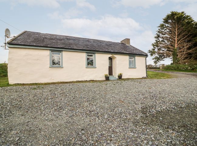 A single story house with three windows and a door with two flower pots outside and a gravel driveway at The Chocolate Box in Ballydehob County Cork