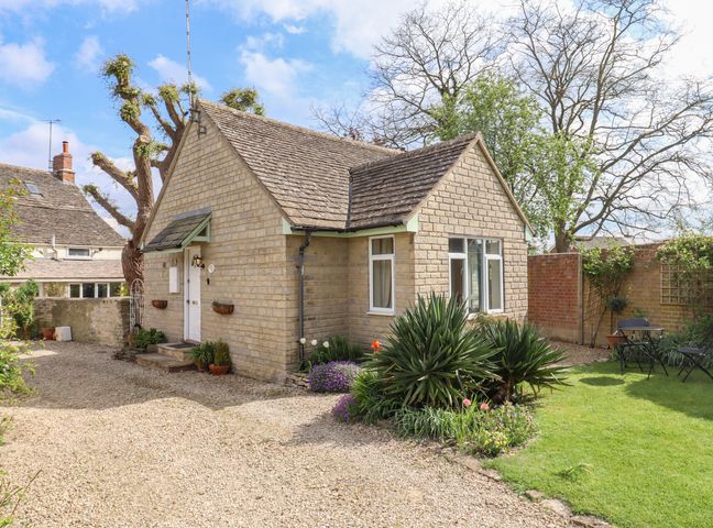 A stone cottage with a gravel driveway and garden with outdoor furniture at Straw Cottage in Cricklade