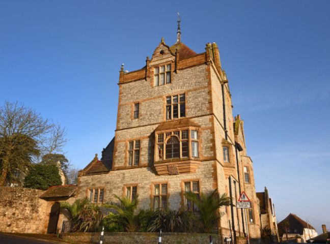 A stone building with multiple windows and a tower under a clear sky at 5 Coram Tower in Lyme Regis