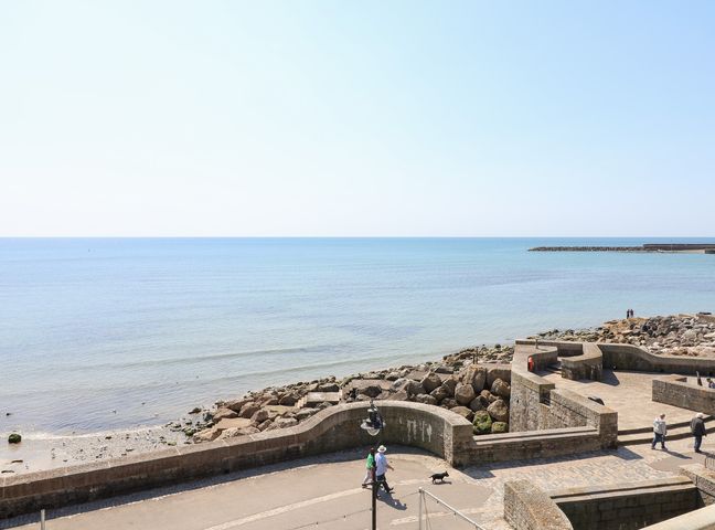 A seaside view with a promenade and people walking at Watersmeet Lyme Regis