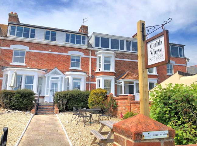 A brick house with white framed windows and a patio area with tables and chairs at 2 Cobb View in Lyme Regis