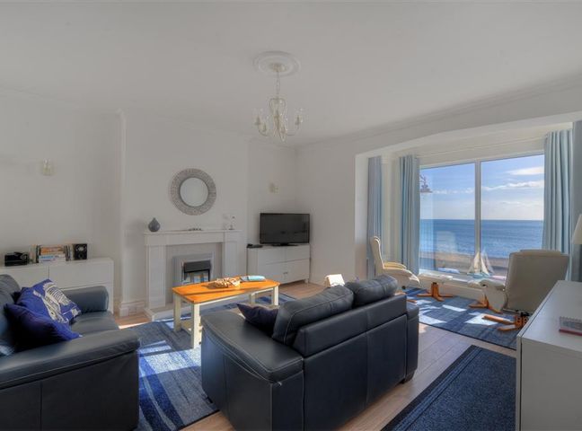 A living room with black leather sofas a wooden coffee table a fireplace a TV and large windows overlooking the sea at 2 Mareeba in Seaton