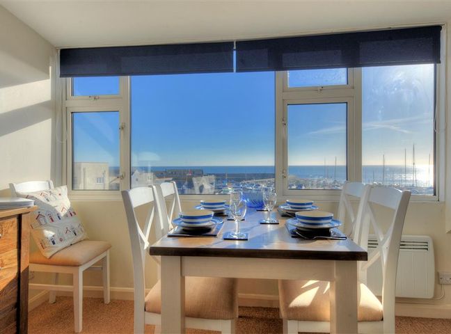 A dining room with a table set for six near large windows overlooking a marina and the sea at Halyards La Casa Lyme Regis