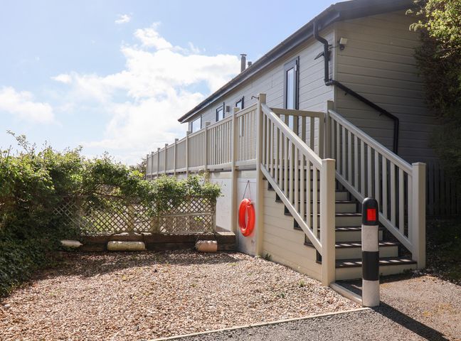 Exterior of a building with a staircase and railing leading to a raised entrance with greenery and gravel ground at High Bullen Lodge in Morcombelake