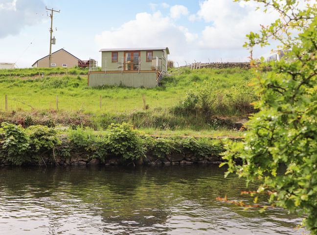 A small green building on a grassy hill overlooking a body of water at Llety'r Bugail 1 in Llanrug