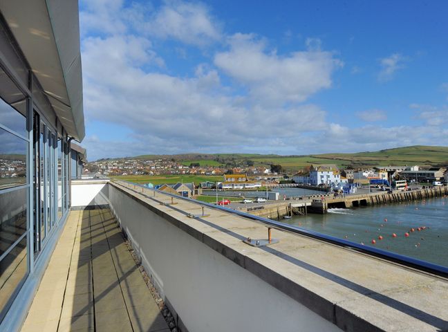 A balcony with a railing and glass doors overlooking a harbor and buildings at The Penthouse in West Bay