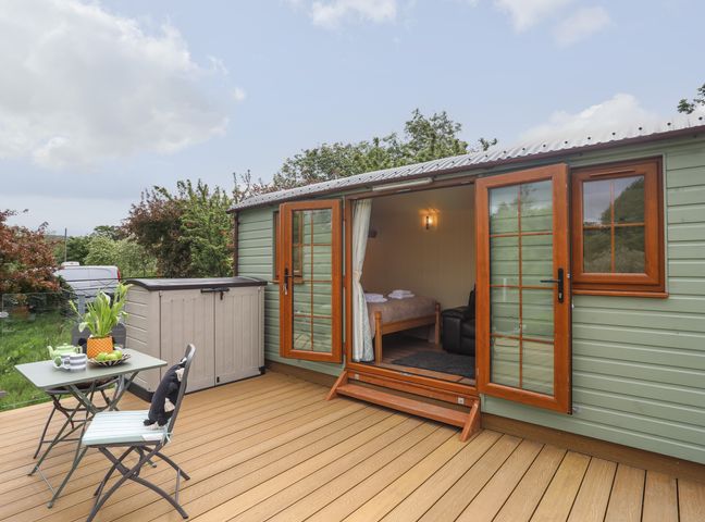 An outdoor deck with table, chairs, storage box, and open door to a small room at Llety'r Bugail 2 in Llanrug