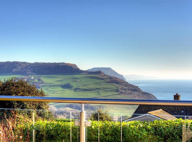 A coastal landscape with green hills sea and rooftops seen from behind a glass balcony at Pendower in Charmouth