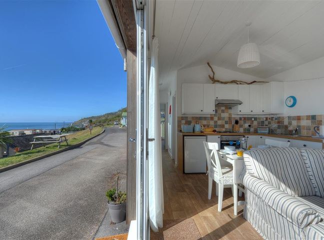 A kitchen and dining area with white cabinets and striped sofa at The Beach Hut in Lyme Regis