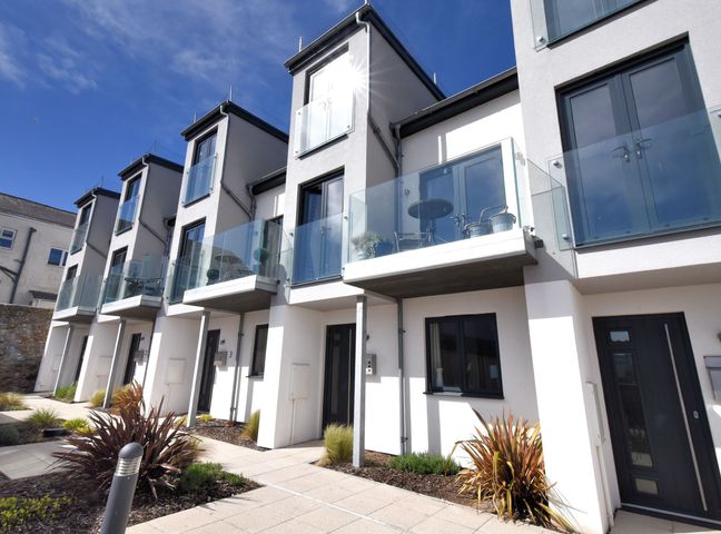 A row of modern townhouses with glass balconies and black doors with plants and paved walkway in front at 3 Grove Mews in Seaton Devon