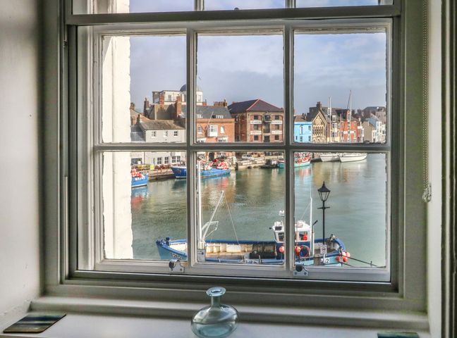 A window looking out onto a harbor with fishing boats and buildings at Embassy Brewers Quay Harbour