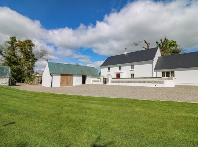 A white house with a red door and detached garage on a gravel driveway with green lawn and trees at Yew Tree House Enniscorthy County Wexford