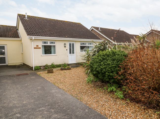 A single-story house with a tiled roof and white door with bushes and gravel in the front garden at Dunes View in Cubert