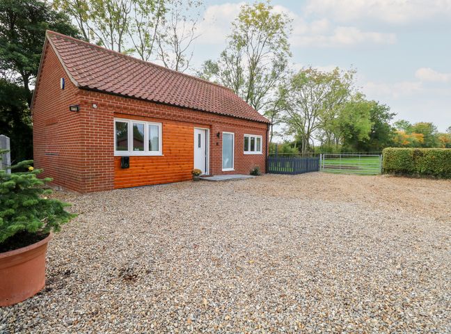 A brick house with a tiled roof and a gravel driveway with trees and a metal gate at Robins Nest in Brisley near North Elmham