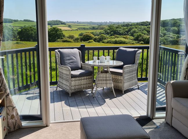 A balcony with two chairs and a table with cups and teapot overlooking green fields at Vendee Lodge Thorness Bay Holiday Park near Cowes