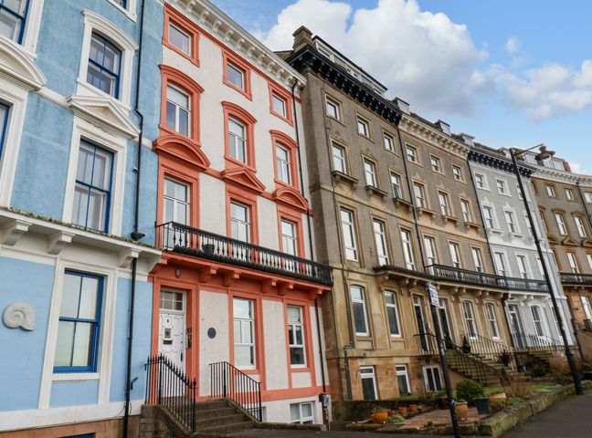 A row of multi-story terrace houses with various facade colors including blue, red, brown, and white on a street with a sidewalk
