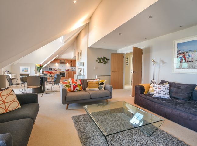 A living room with sofas pillows glass coffee table and an open kitchen at 13 Buckfields in Lyme Regis