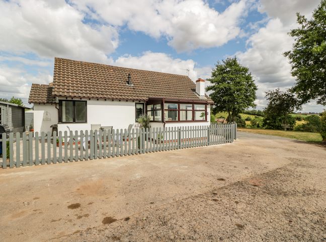 A single-story house with a tiled roof and fenced patio area surrounded by trees and open land at Phocle Ridge in Phocle Green near Ross-On-Wye