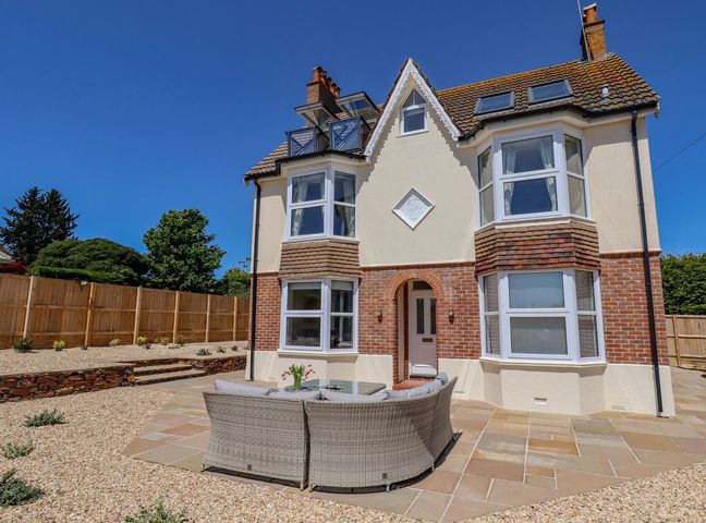 A patio with outdoor seating in front of a two story house with bay windows at Temple House in Sidmouth