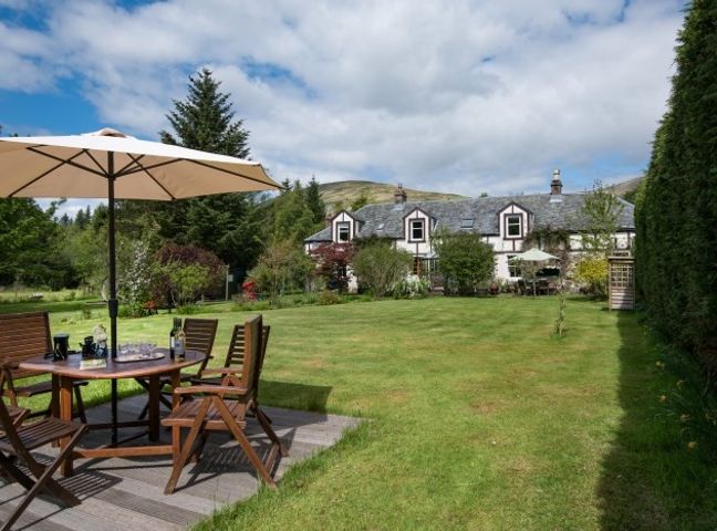 A backyard with wooden patio furniture and an umbrella in front of a house at Strone House in Loch Lomand & Trosschs National Park