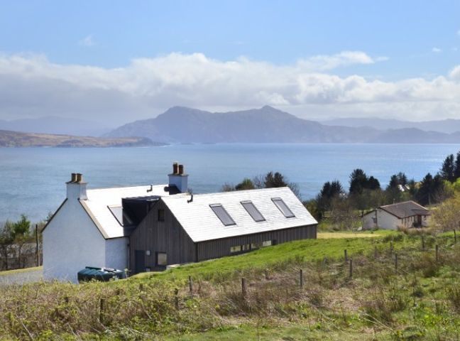 A house with multiple skylights on the roof overlooking a body of water and mountains at Teangue House Sleat nr Armadale