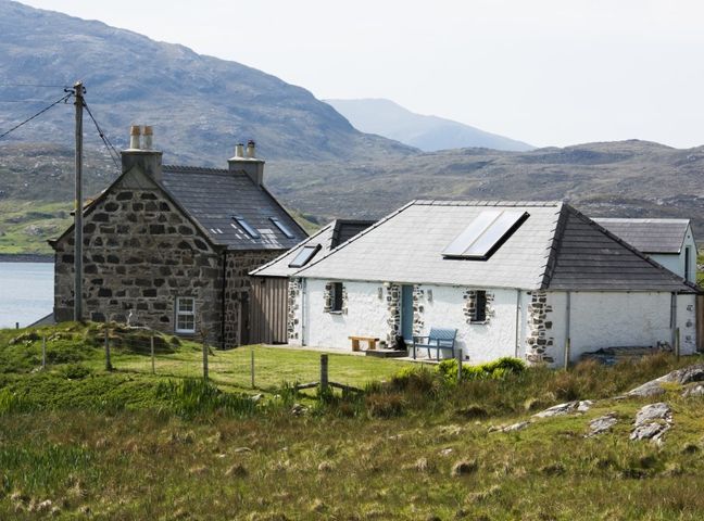 A stone house and a white cottage with skylights in a rural landscape with hills and water at The Barn at Reef in Timsgearraidh
