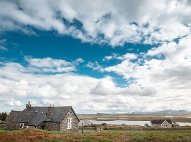 A stone house with a slate roof near a body of water and hills at Achmore Schoolhouse in Achmore near Stornoway