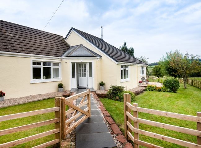 A pathway leading to a cream colored house with a wooden gate and green lawn at Gaidrew Cottage in Drymen