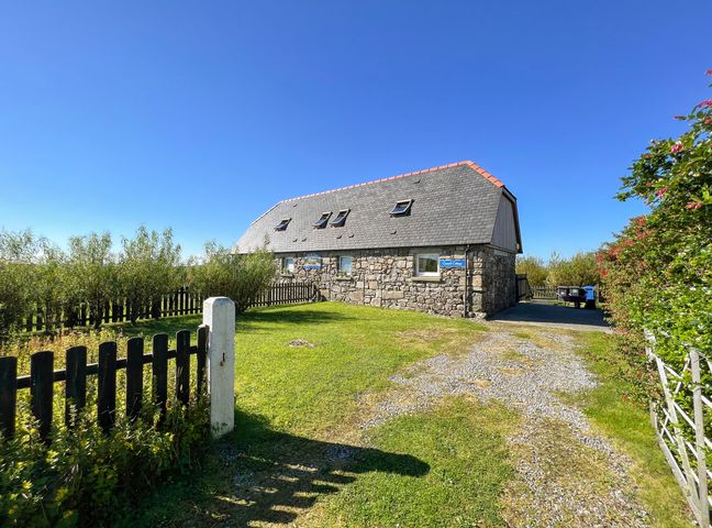A stone cottage with a gravel driveway and fenced garden at Canach Cottage in South Boisdale near Daliburgh