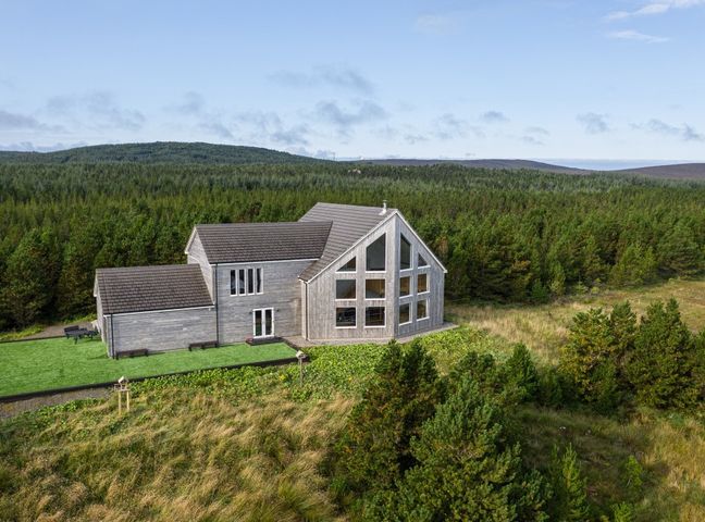 A two-story house with large windows surrounded by grass and trees at Constant & True Seasmhach agus Dileas in Claddach Vallay Sollas North Uist