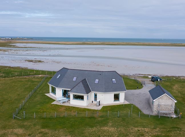 A house with a fenced yard near a beach and a small outbuilding at Gualan Sands in Iochdar