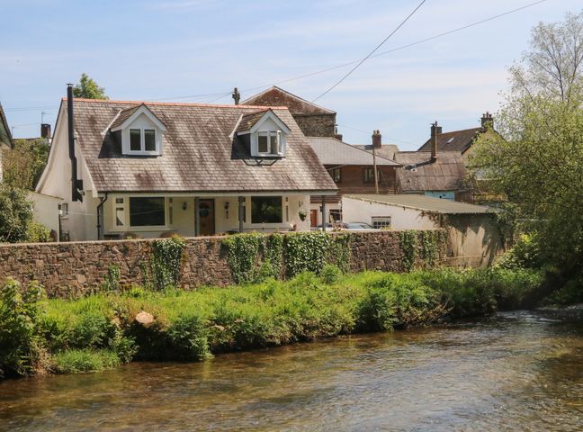 A house with a sloped roof behind a stone wall beside a river at Barleside in Dulverton