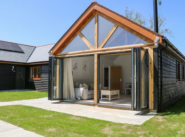 A wooden house with large glass doors opening to a living room with a sofa and a coffee table at Robins Nest in Titchfield Common