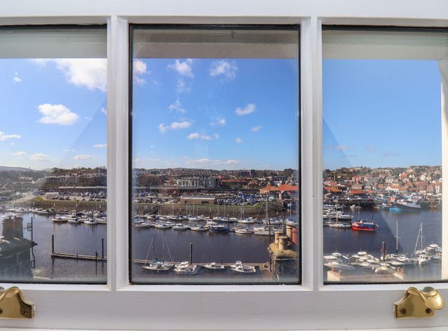 A view of a marina with boats and buildings seen through a window at Navigators Rest in Whitby