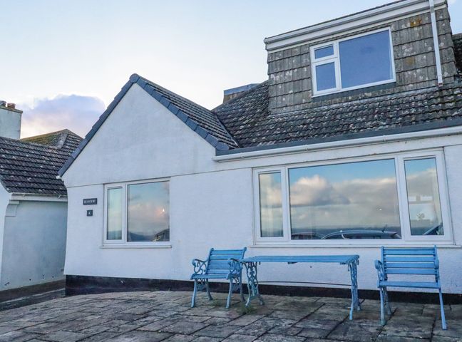 The exterior of a white house with a tiled roof two blue benches and a blue table on a stone patio at Sea View in Mevagissey