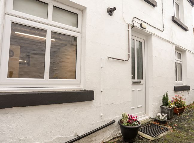 An exterior wall of a building with a white door and two windows with flower pots on the ground at Llys Mair in Llanderfel near Bala