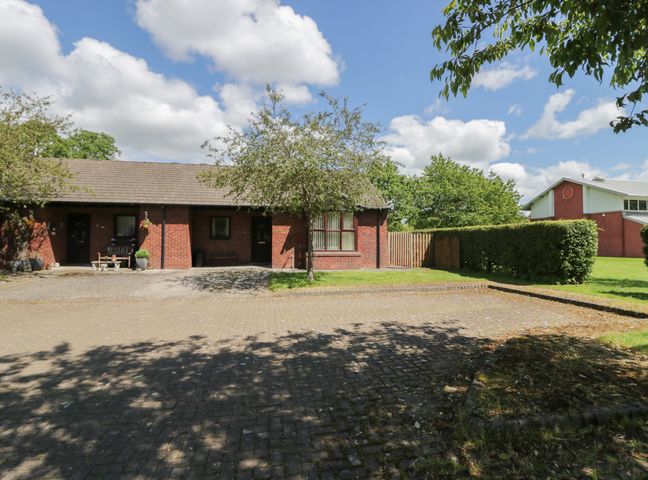 A brick house with two doors and windows in front of a paved driveway with trees and bushes at 21 Eamont Park Penrith