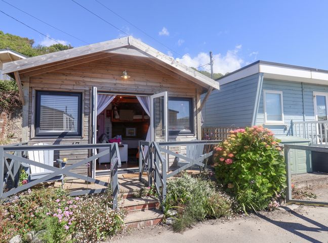 A wooden cabin with open doors and a small garden in front at Sea Spray in Lyme Regis