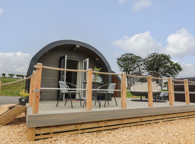 A wooden pod with an outdoor deck with two chairs a round table and a hanging chair at Laird Lodge 4 in Lochmaben