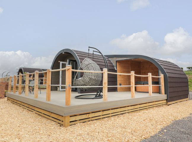 An outdoor deck with a hanging chair and seating area in front of curved wooden pods at Laird Lodge 5 in Lochmaben