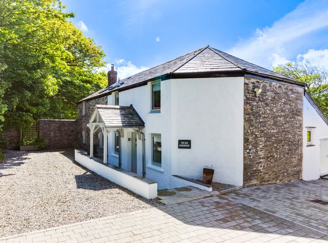 Exterior view of a two-story house with white and stone walls small porch and gravel driveway at The Old Bakehouse - within the Helland Barton Farm collection Delabole