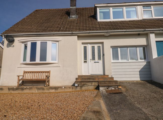 The front exterior of a house with a bench near a bay window a white door and steps leading to the entrance at Sandtop in Tenby