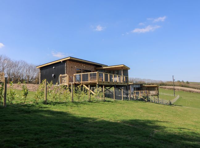 A modern wooden house with a deck on a grassy hill with a fence at Bryn Hafod in Llandrindod Wells